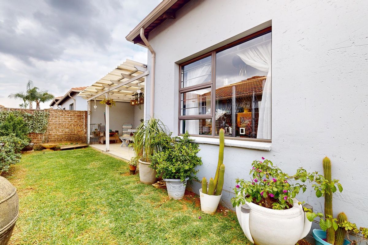 Rear view of the townhouse featuring a small lawn, a covered patio area, and a brick boundary wall.