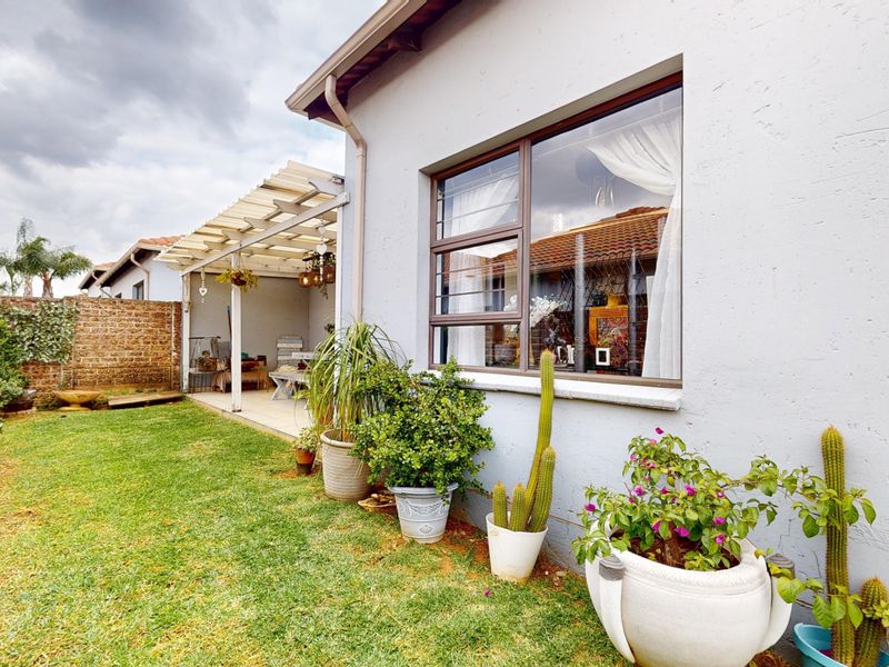 Rear view of the townhouse featuring a small lawn, a covered patio area, and a brick boundary wall.