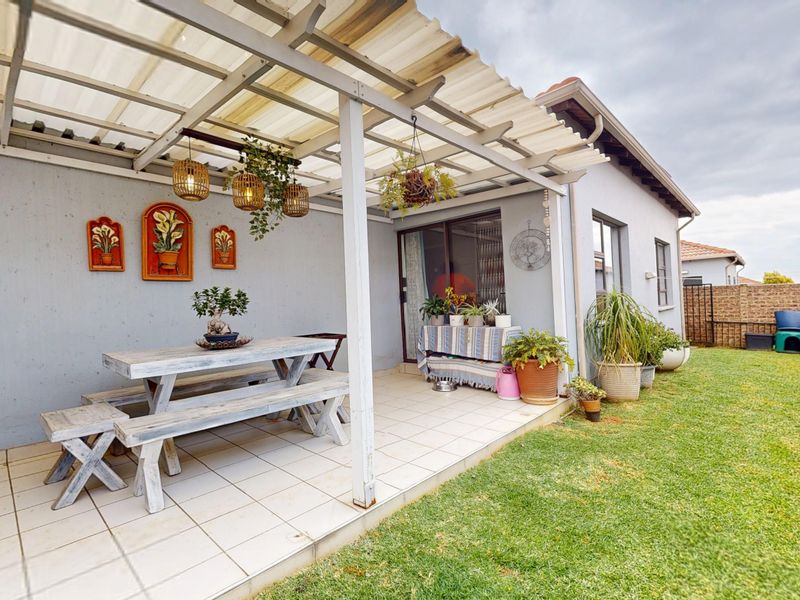 A covered outdoor patio area with tiled flooring, featuring a corrugated roof structure and direct access to the garden through sliding glass doors.