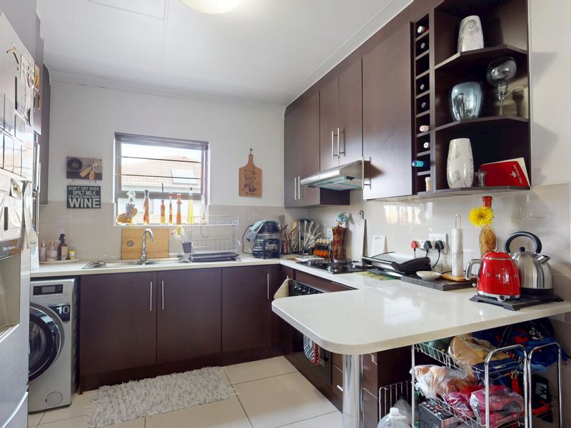 A functional kitchen featuring dark wood cabinetry, stone countertops, a built-in hob with extractor fan, and tiled flooring.