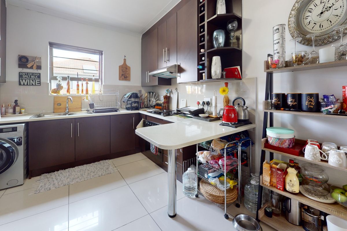 A functional kitchen featuring dark wood cabinetry, light countertops, tiled flooring, and integrated appliances, offering a practical layout for daily meal preparation.