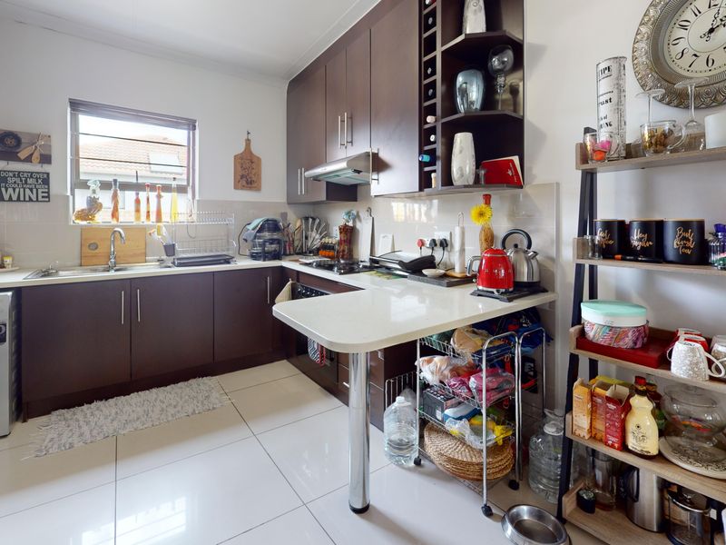 A functional kitchen featuring dark wood cabinetry, light countertops, tiled flooring, and integrated appliances, offering a practical layout for daily meal preparation.