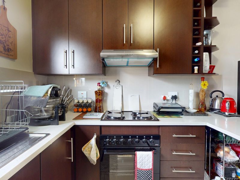 A functional kitchen featuring dark wood cabinetry, a built-in oven with electric hob, extractor fan, and a stainless steel sink with tiled backsplash.