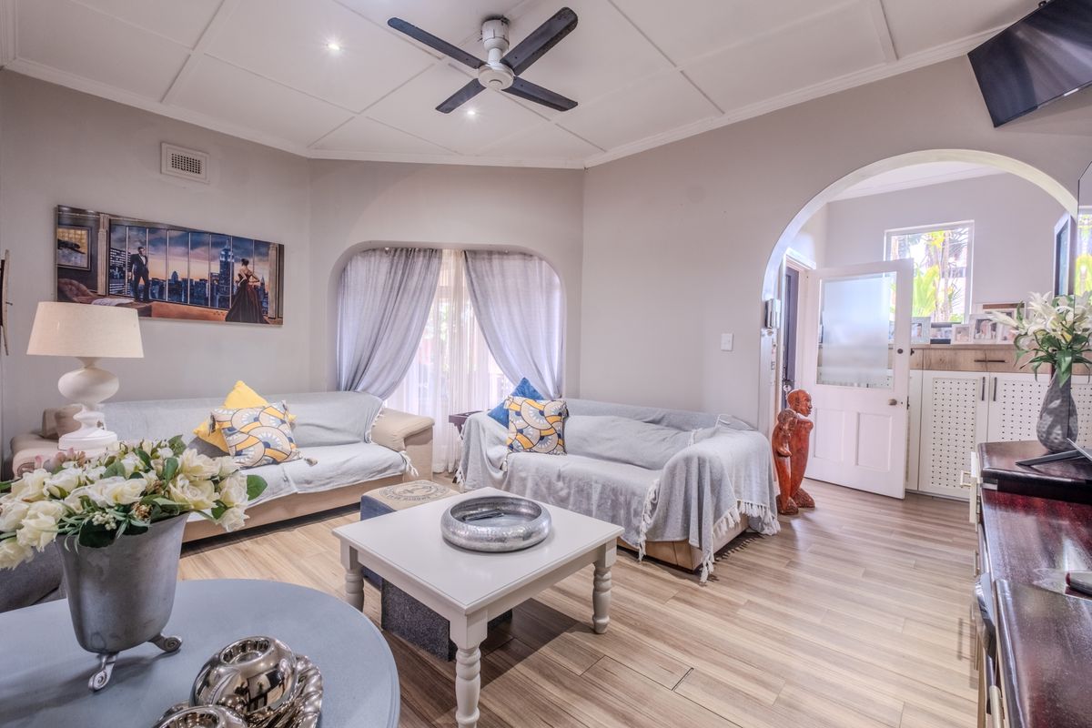 A well-maintained living room featuring laminate flooring, a ceiling fan, and a distinctive arched entryway leading to the home's entrance.