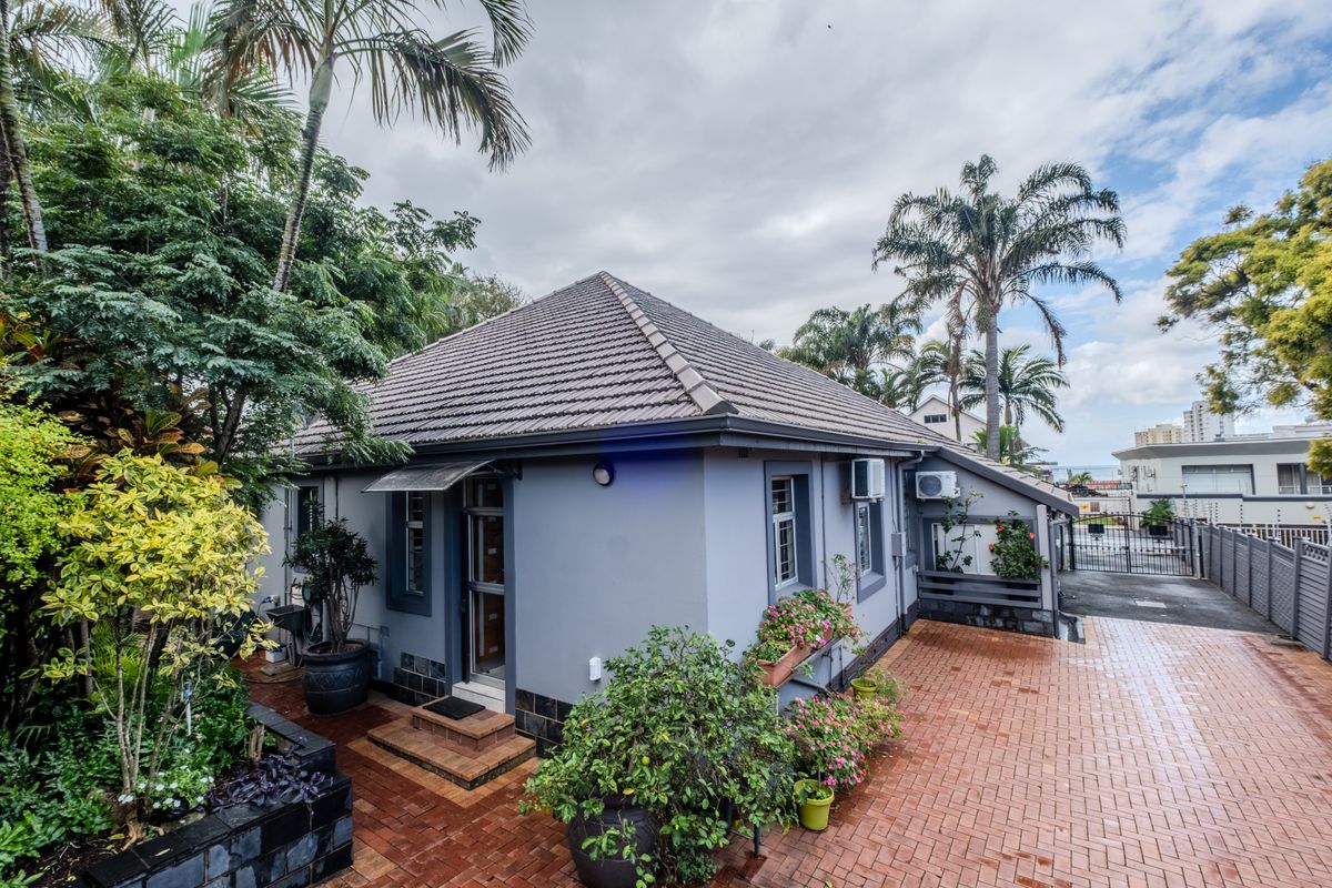 A well-maintained rear exterior view featuring a tiled roof, brick paved courtyard, and established garden surroundings with secure gated access.