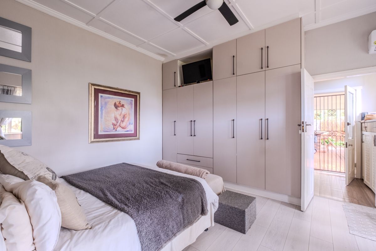 A well-maintained bedroom featuring extensive built-in cabinetry, a ceiling fan, and light-toned laminate flooring, with direct access to an outdoor area.