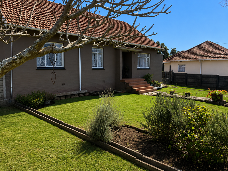 A well-maintained front exterior of a brick house featuring a tiled roof, security-barred windows, and a neat, landscaped garden with concrete steps.