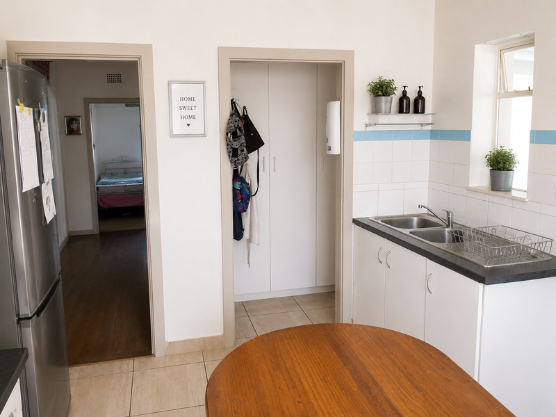 A functional scullery area featuring a double bowl sink, tiled splashback, and built-in storage cabinetry with direct access to adjacent rooms.