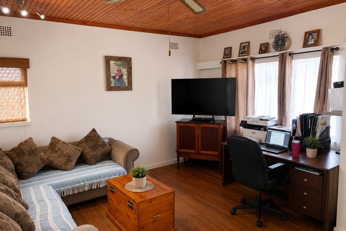 A living room featuring warm timber ceiling paneling, polished timber flooring, and a ceiling fan, creating a cozy and traditional atmosphere.