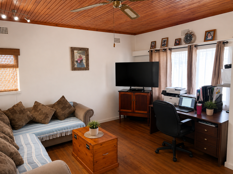 A living room featuring warm timber ceiling paneling, polished timber flooring, and a ceiling fan, creating a cozy and traditional atmosphere.