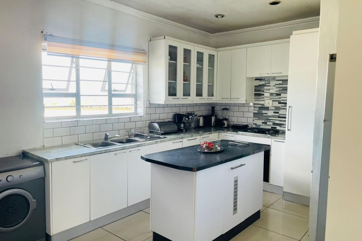 A functional kitchen featuring white cabinetry, a central island, tiled backsplash, and built-in appliances, offering a practical layout for daily cooking and preparation.