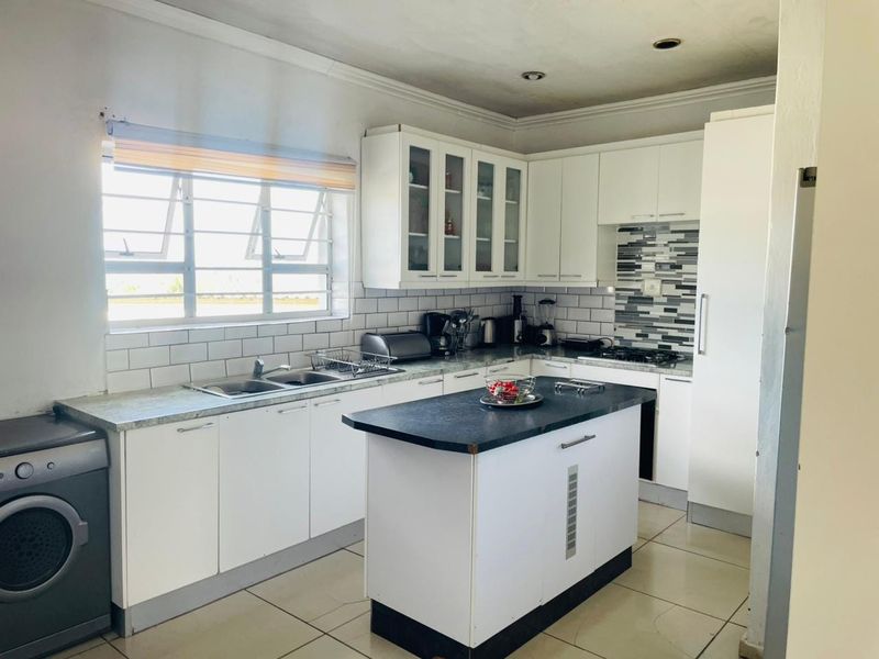 A functional kitchen featuring white cabinetry, a central island, tiled backsplash, and built-in appliances, offering a practical layout for daily cooking and preparation.