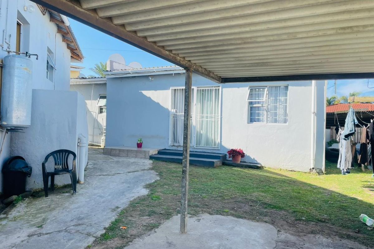 Rear exterior view of the property featuring a corrugated metal carport, concrete paved area, small lawn, and access to the home via sliding doors.