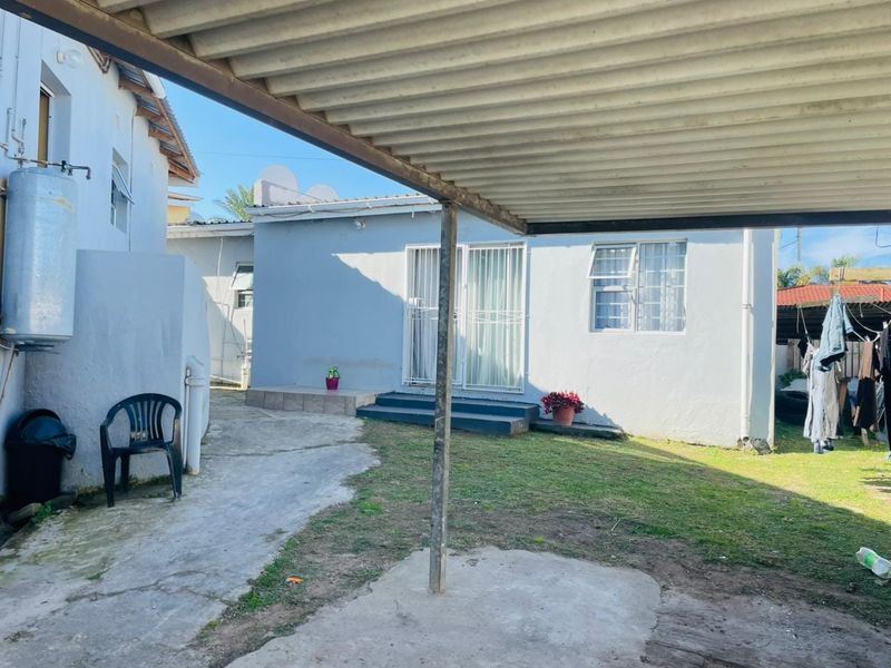 Rear exterior view of the property featuring a corrugated metal carport, concrete paved area, small lawn, and access to the home via sliding doors.
