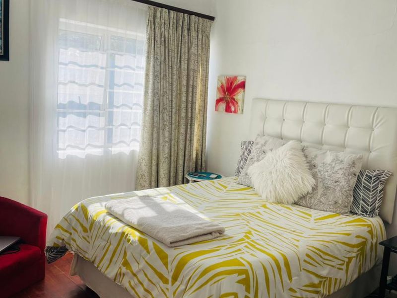 A bedroom featuring timber flooring and a window with curtain treatments. The space includes a visible crack in the ceiling cornice.