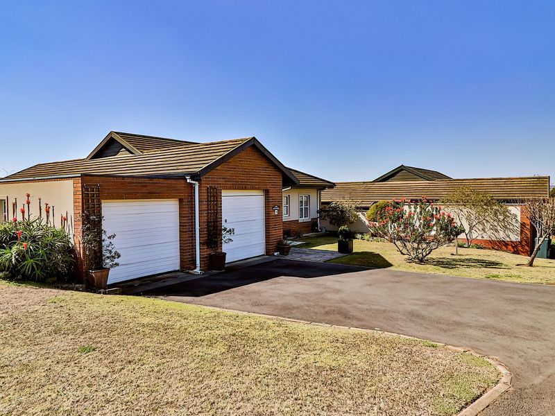 Front exterior view of a brick house featuring a double garage, tiled roof, and an asphalt driveway set within a landscaped garden.
