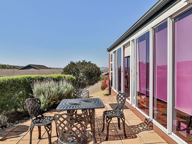 A paved outdoor patio area featuring large sliding glass doors with integrated external roller blinds, offering a clear view of the surrounding landscape.
