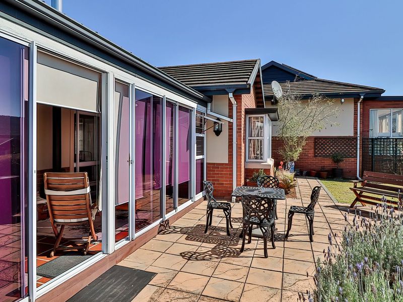 A paved outdoor patio area featuring sliding glass doors leading into the home, set against a brick exterior with a tiled roof.