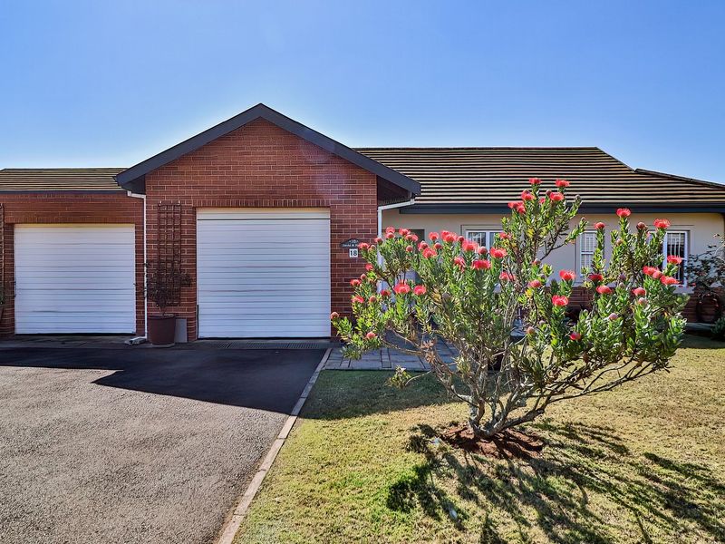 Front view of a well-maintained single-story brick house featuring a double garage, tiled roof, and a neat front garden with a paved driveway.