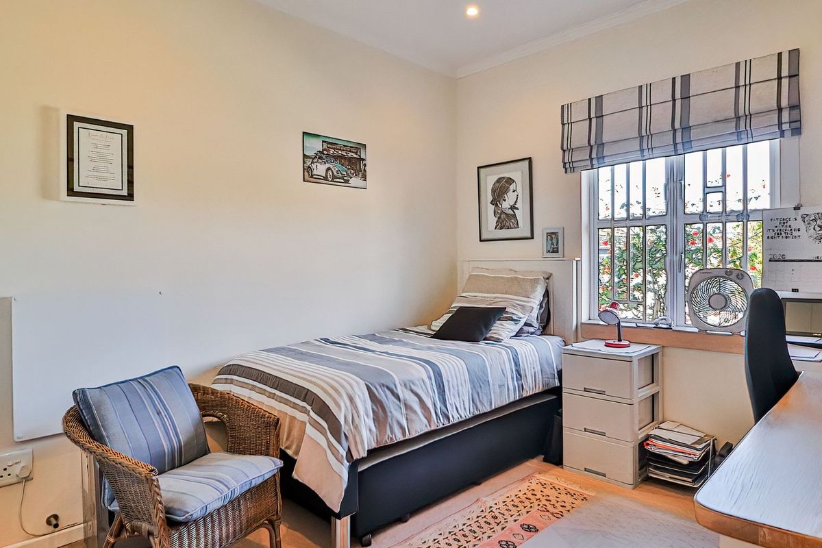 A well-lit bedroom featuring a window with security bars, a roman blind, and recessed downlighting, providing a functional and comfortable living space.