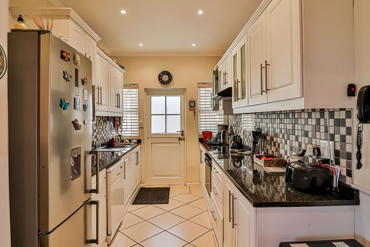 A well-maintained galley-style kitchen featuring white cabinetry, dark granite countertops, a tiled backsplash, and integrated appliances with direct access to the exterior.