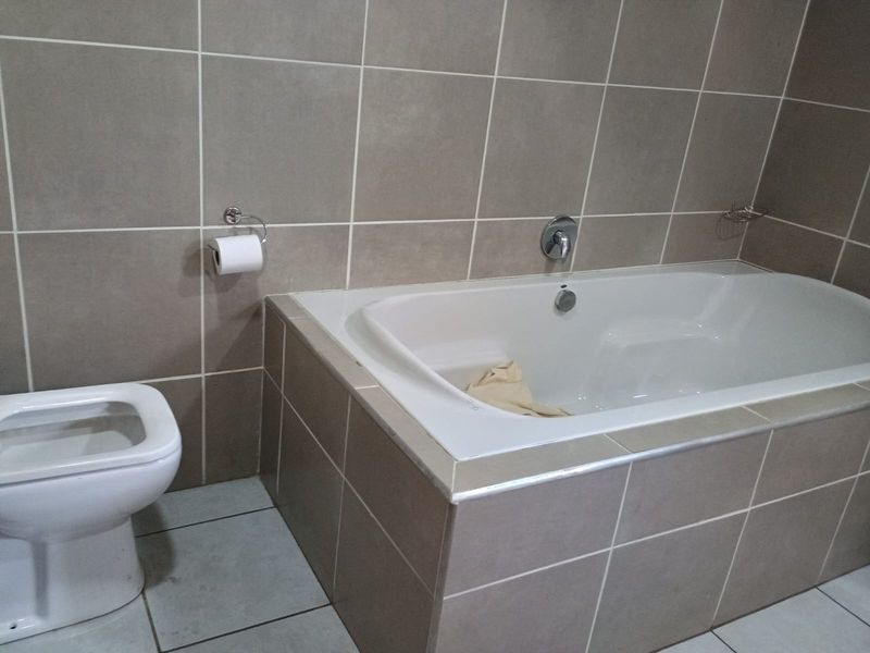 A functional bathroom featuring a built-in bathtub with chrome fixtures and neutral wall and floor tiling.