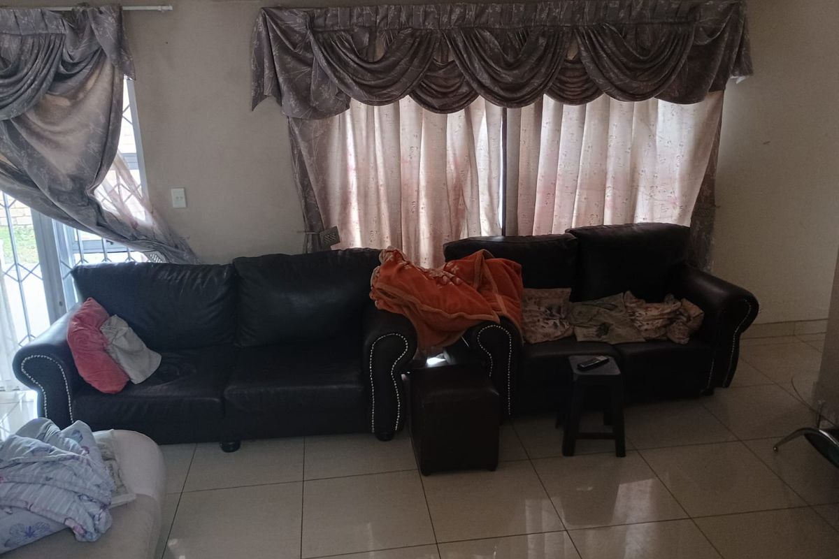 A living room featuring tiled flooring, a sliding glass door with security gate, and decorative window treatments.