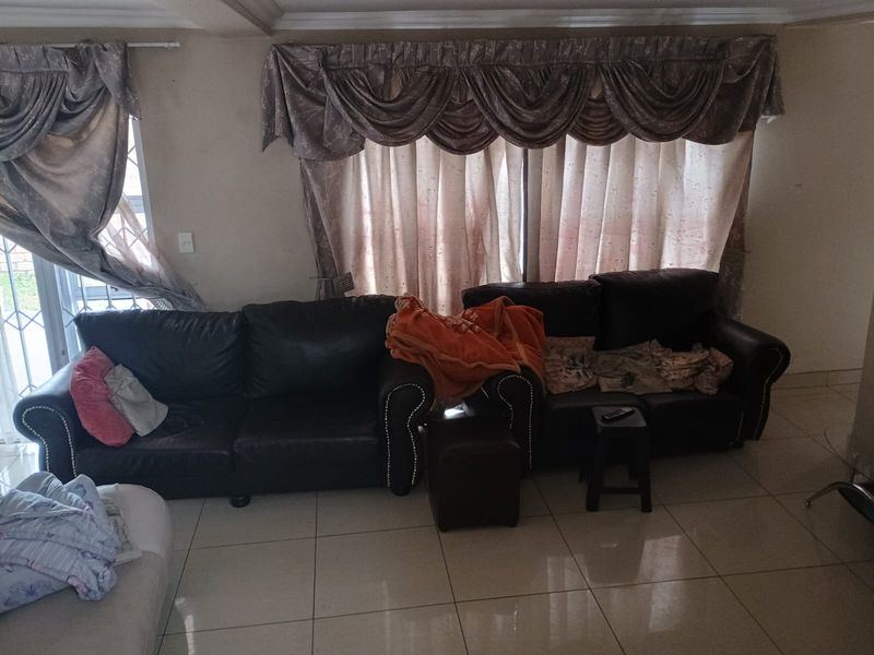 A living room featuring tiled flooring, a sliding glass door with security gate, and decorative window treatments.