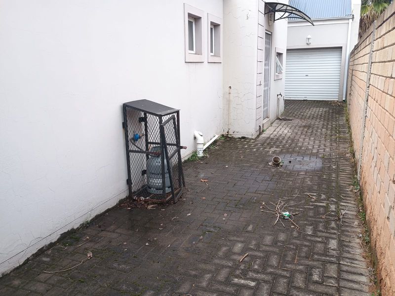 Rear exterior area featuring paved flooring, a gas cylinder storage cage, and access to the garage, showing signs of wear and maintenance requirements.