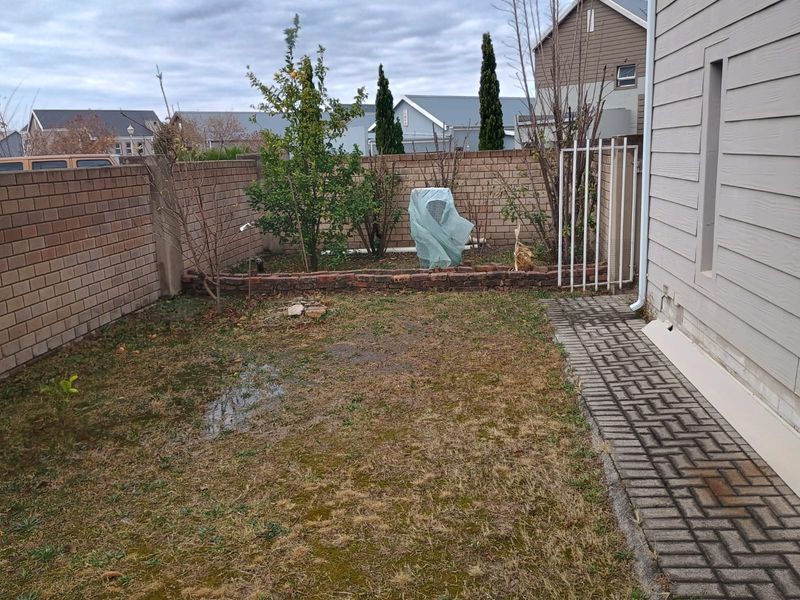 A rear garden area featuring a paved walkway, brick boundary walls, and a raised garden bed, currently requiring landscaping maintenance.