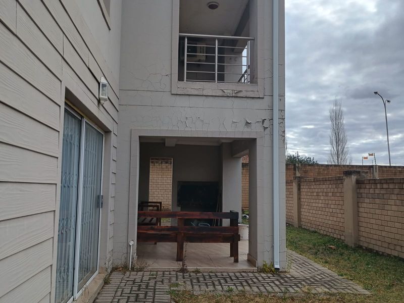 Covered ground floor patio featuring a built-in braai, adjacent to a small balcony above, showing significant exterior wall paint deterioration and cracking.