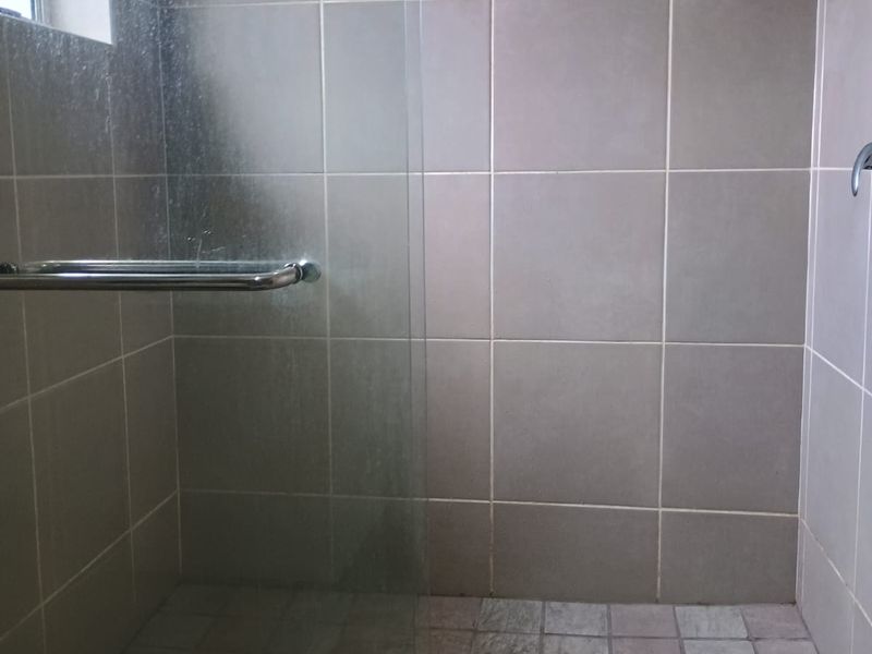 A functional walk-in shower featuring neutral wall tiling, a glass screen, and a tiled floor area.