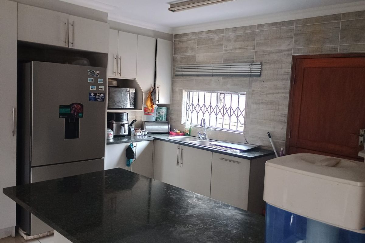 A functional kitchen featuring built-in cabinetry, granite countertops, a double basin sink, and tiled backsplash with a security-fitted window.