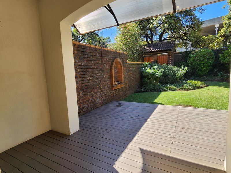 A covered timber deck patio overlooking a private landscaped garden with a feature face brick boundary wall.