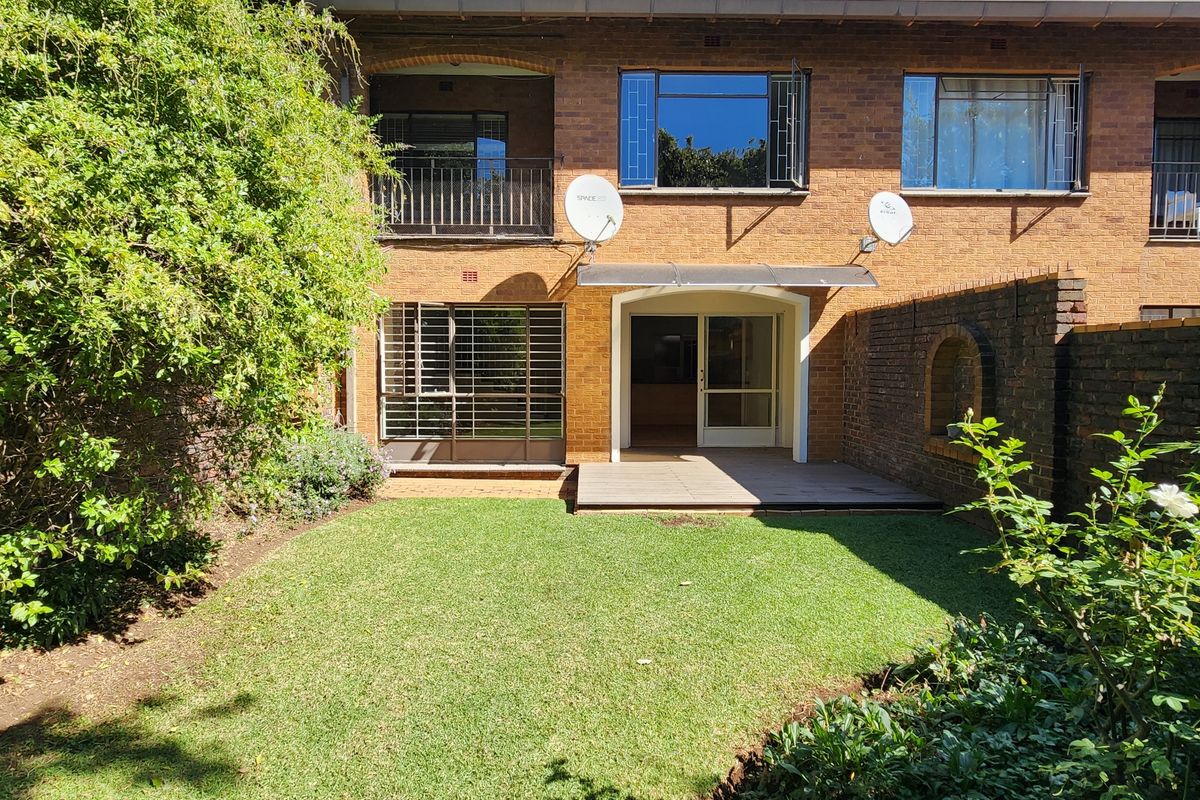 Rear view of a brick townhouse featuring a private garden, timber deck, and upper-level balcony with security features.