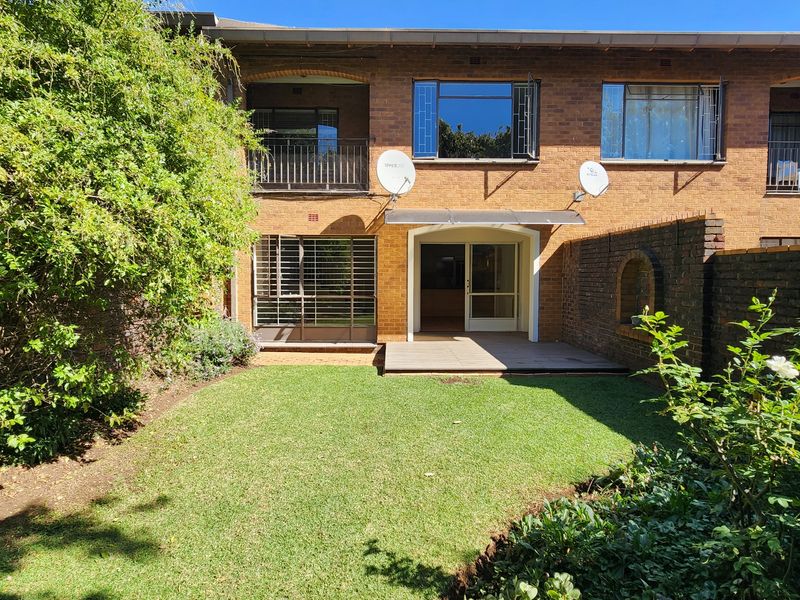 Rear view of a brick townhouse featuring a private garden, timber deck, and upper-level balcony with security features.