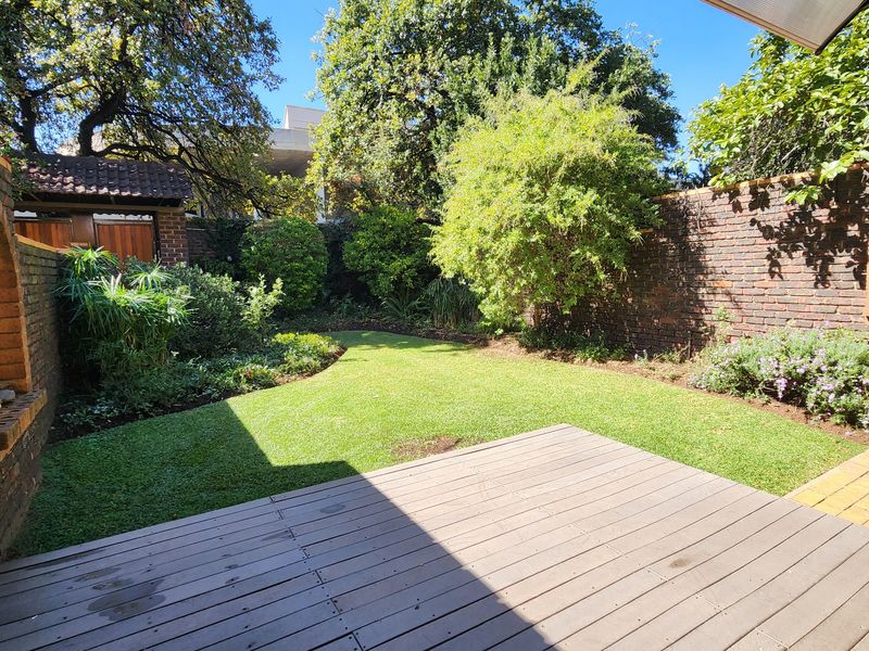 A private rear garden featuring a timber deck, well-maintained lawn, and established perimeter brick walls with mature landscaping.