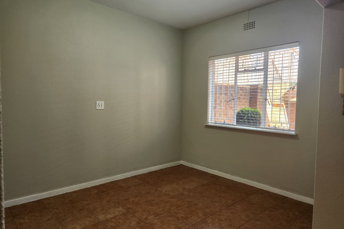 A clean, empty bedroom featuring neutral wall paint, tiled flooring, and a window with fitted blinds.