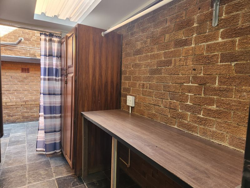 A functional laundry area featuring exposed brick walls, slate flooring, built-in cabinetry, and a practical work surface under a translucent roof.