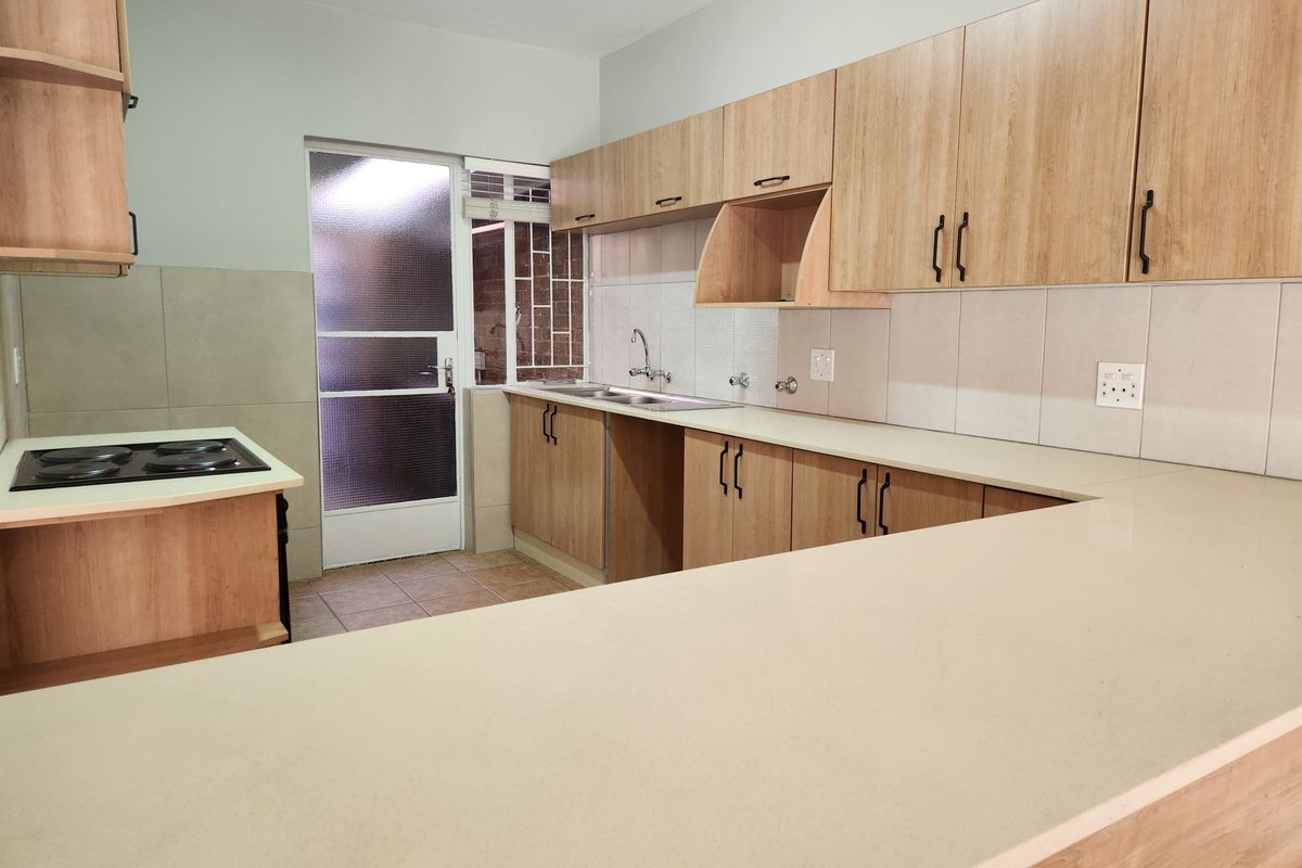 A clean, modern kitchen featuring light wood-finish cabinetry, ample countertop space, a built-in electric hob, and direct access to an exterior area.