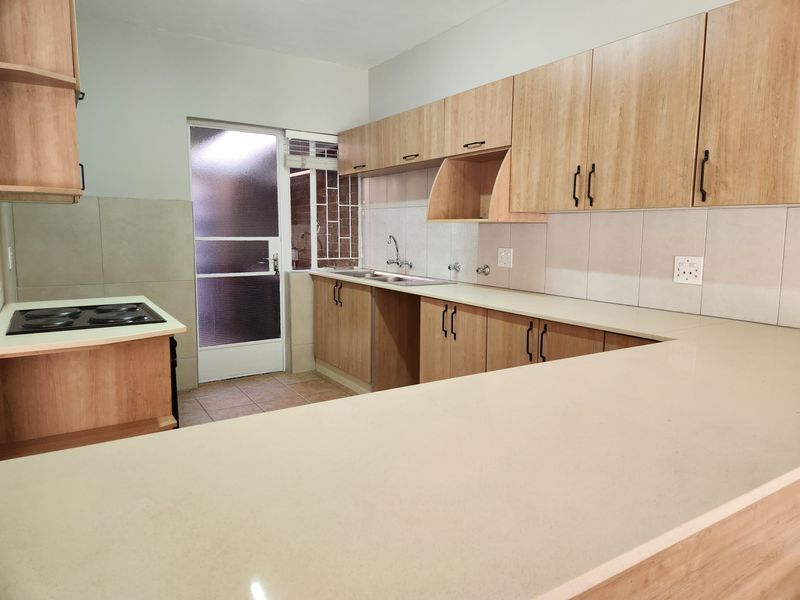A clean, modern kitchen featuring light wood-finish cabinetry, ample countertop space, a built-in electric hob, and direct access to an exterior area.