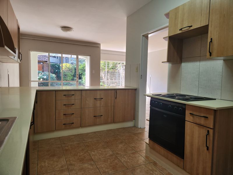 A functional kitchen featuring wood-finish cabinetry, built-in oven and stove, tiled flooring, and a breakfast counter overlooking the living area.