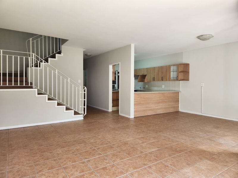 Spacious open-plan living area featuring tiled floors, a staircase with metal balustrade, and a functional kitchen with built-in cabinetry and a breakfast bar.