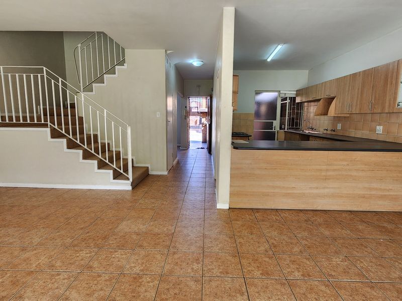 Open-plan living area featuring a staircase with metal balustrade, tiled flooring, and a functional kitchen with wood-look cabinetry and dark countertops.