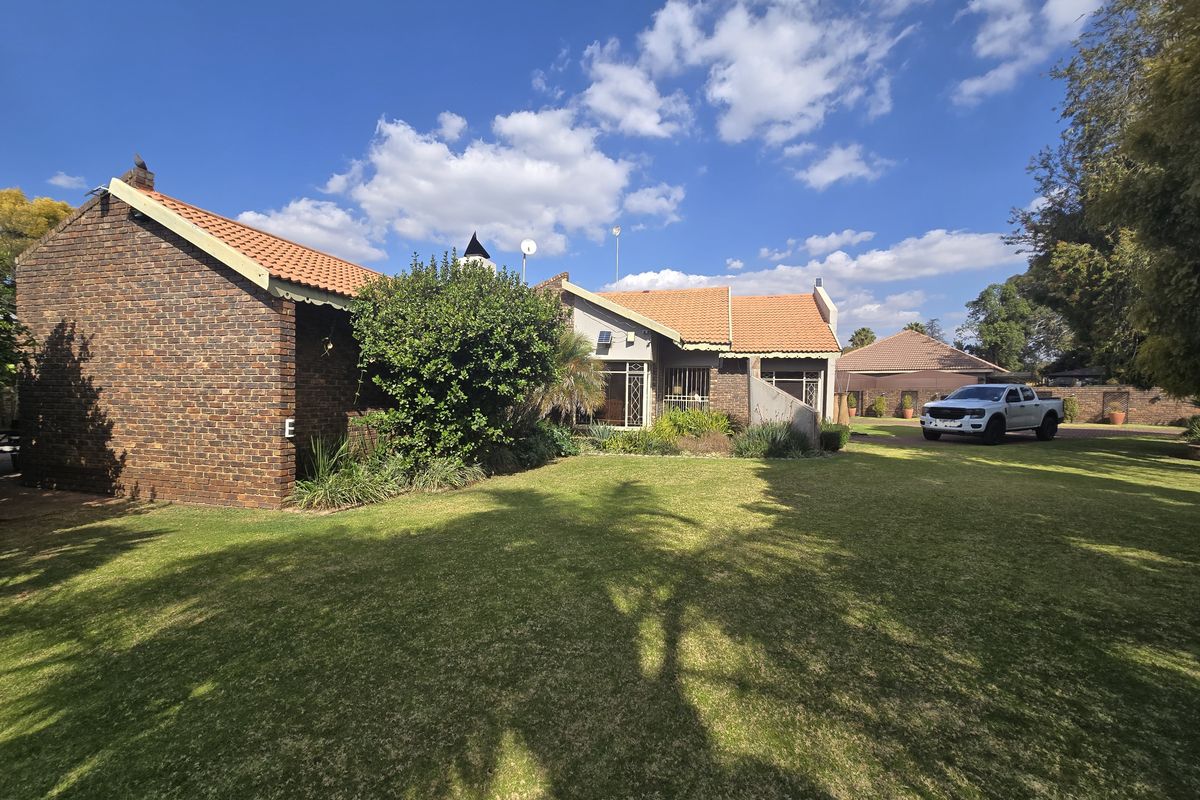 A view of the rear of the house featuring a face brick facade, terracotta roof tiles, and a well-maintained lawn.