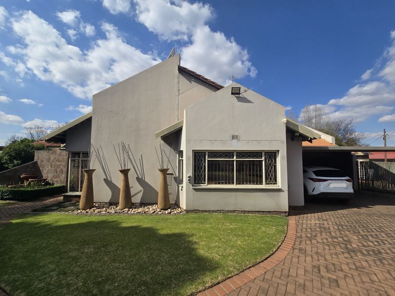 Front elevation of a well-maintained house featuring a paved driveway, carport, and landscaped front garden with secure window treatments.