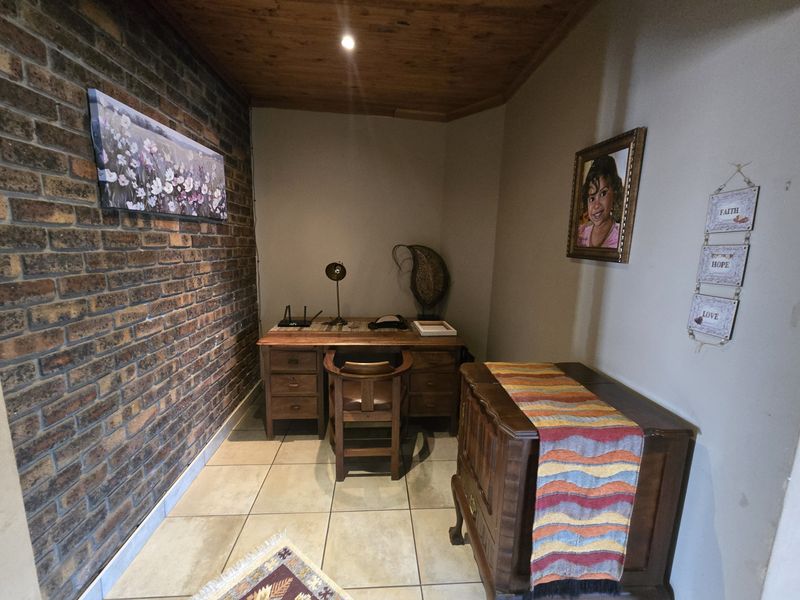 A compact home office featuring an exposed brick feature wall, timber ceiling, and tiled flooring, providing a functional workspace.