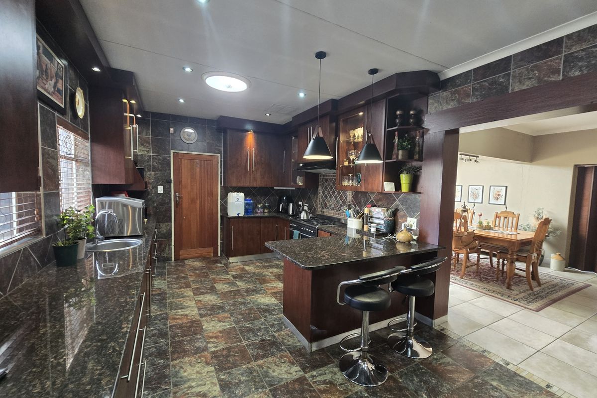 Spacious kitchen featuring dark wood cabinetry, granite countertops, a breakfast bar, and integrated appliances, flowing into an adjacent dining area.