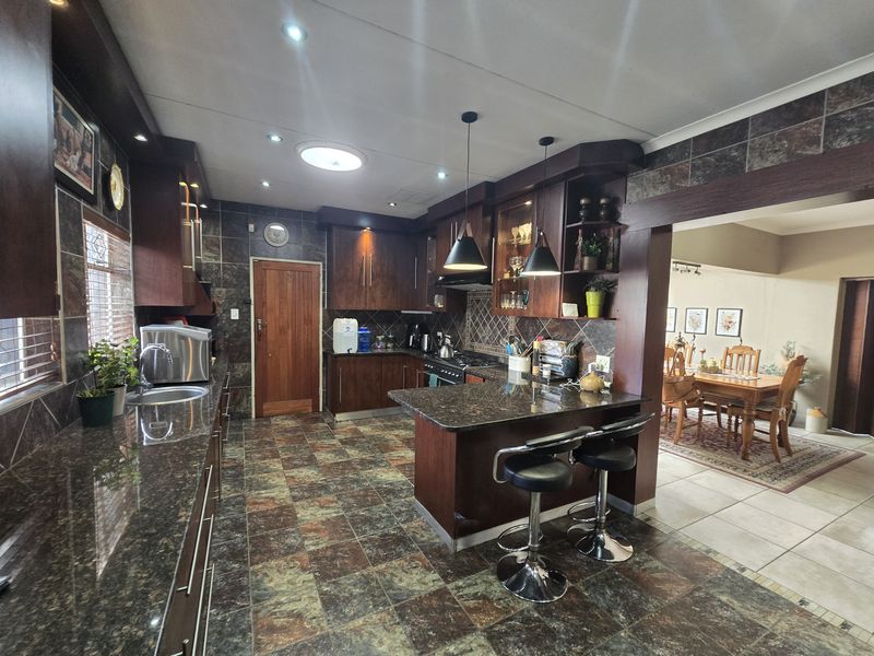 Spacious kitchen featuring dark wood cabinetry, granite countertops, a breakfast bar, and integrated appliances, flowing into an adjacent dining area.