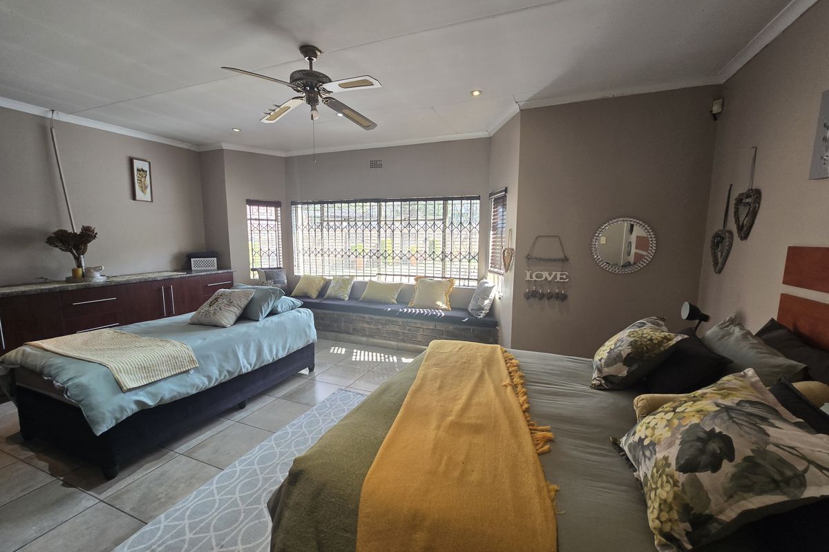 Spacious bedroom featuring tiled flooring, built-in cabinetry, a ceiling fan, and a large window with security bars and a built-in bench seat.